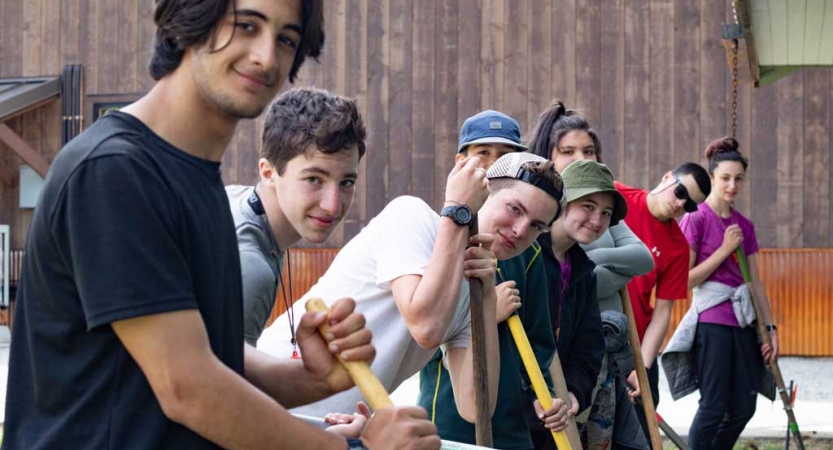 a group of outward bound students stop shoveling to smile at the camera during a service project